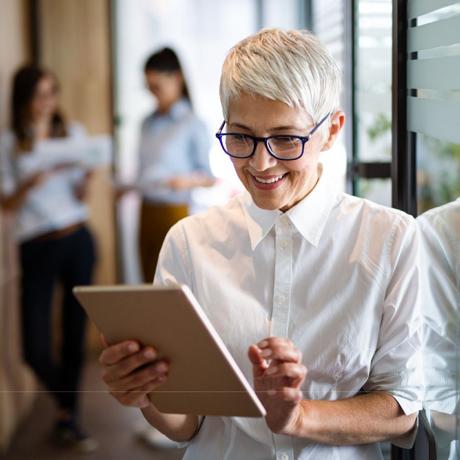 A woman wearing glasses intently examines a tablet device in her hands.