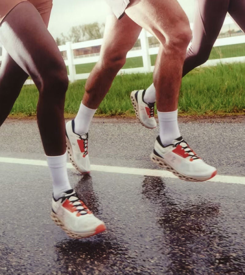 Close-up of runners' legs in motion on a wet road, wearing high-performance running shoes.