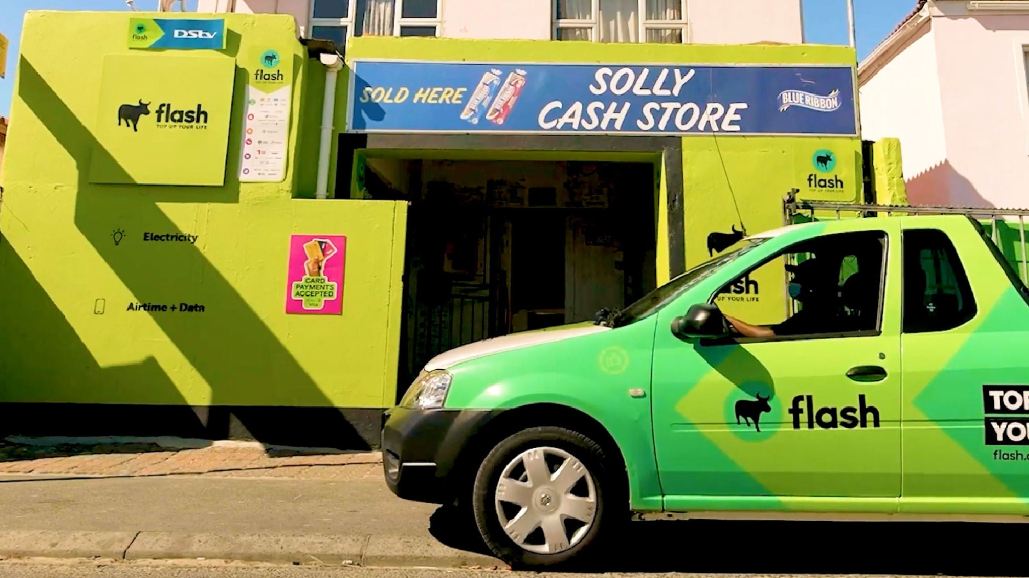Flash logo displayed on storefront and vehicle. A bright green Flash-branded car is parked in front of Solly Cash Store, which features multiple Flash signs and service icons on a lime-green exterior.