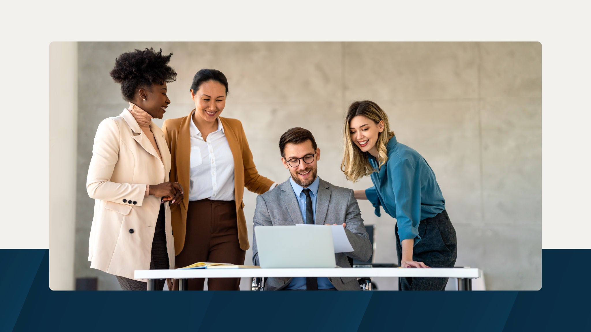 A group of three colleagues standing around a seated coworker who is reviewing documents on a laptop in a bright, modern office setting.