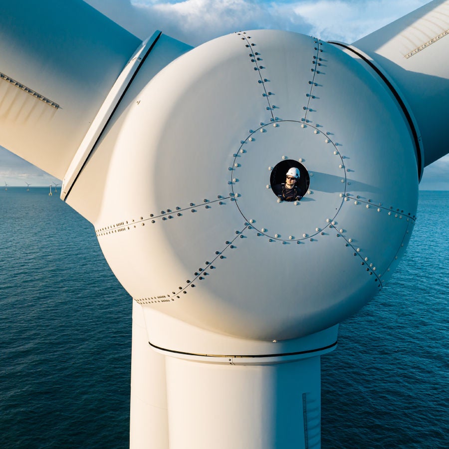 A figure is positioned on the summit of a wind turbine, gazing out over the expansive scenery below.