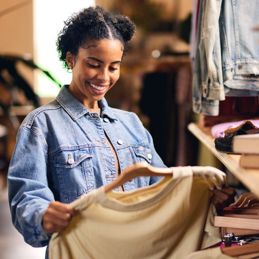 A woman examines a shirt while shopping in a clothing store, showcasing her interest in fashion and style choices.
