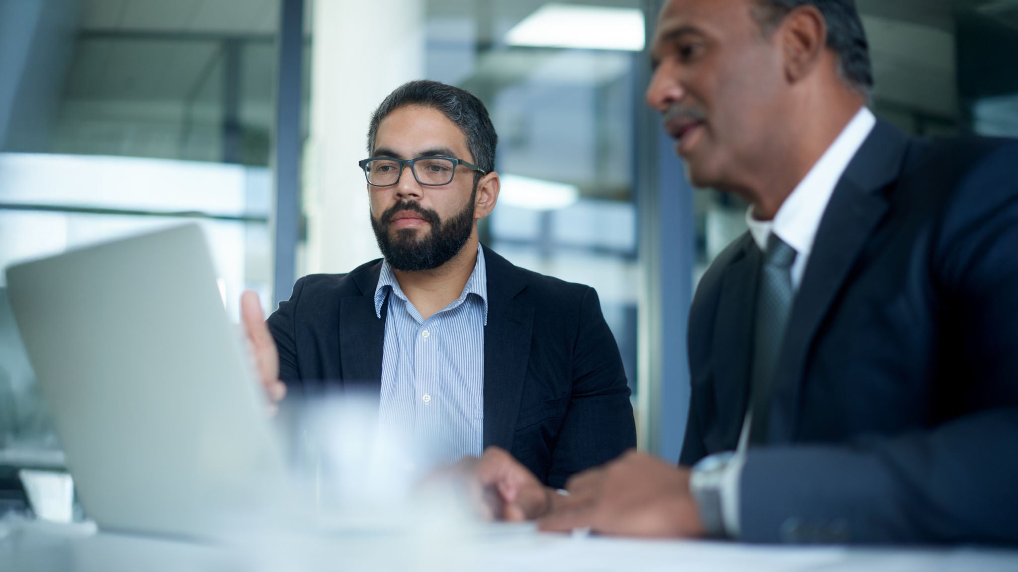 Two professionals seated at a desk reviewing information on a computer screen in a modern office environment.