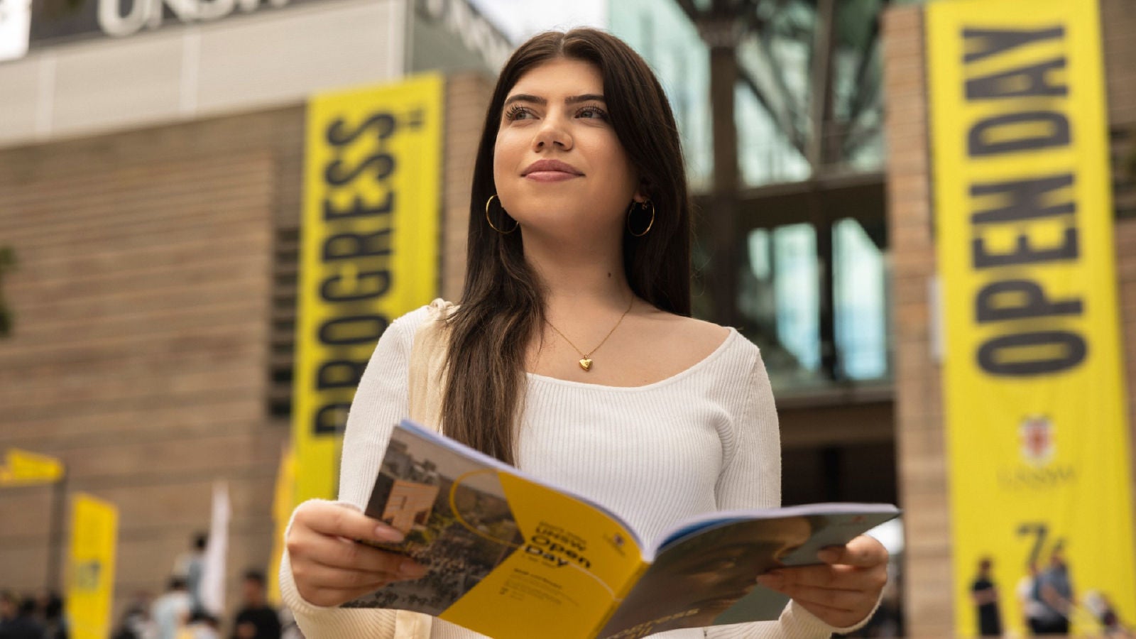 A student holding an Open Day booklet while standing on the UNSW Sydney campus with bright yellow event banners in the background.