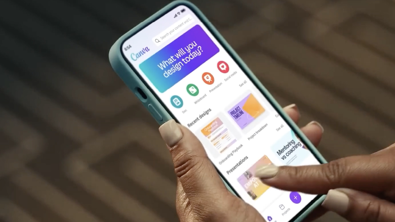 A person holding a smartphone and navigating the Canva app interface showing design options and recent projects.