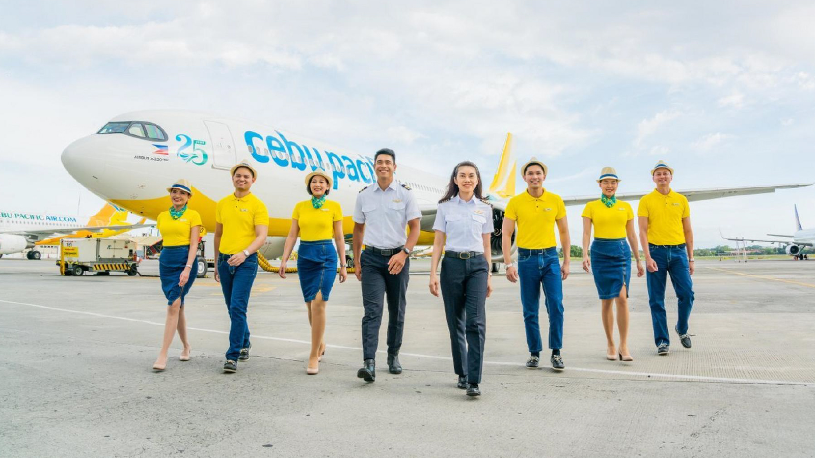 A group of Cebu Pacific airline crew members walking on an airport tarmac in front of a parked aircraft, wearing yellow uniforms, with the airplane visible in the background.