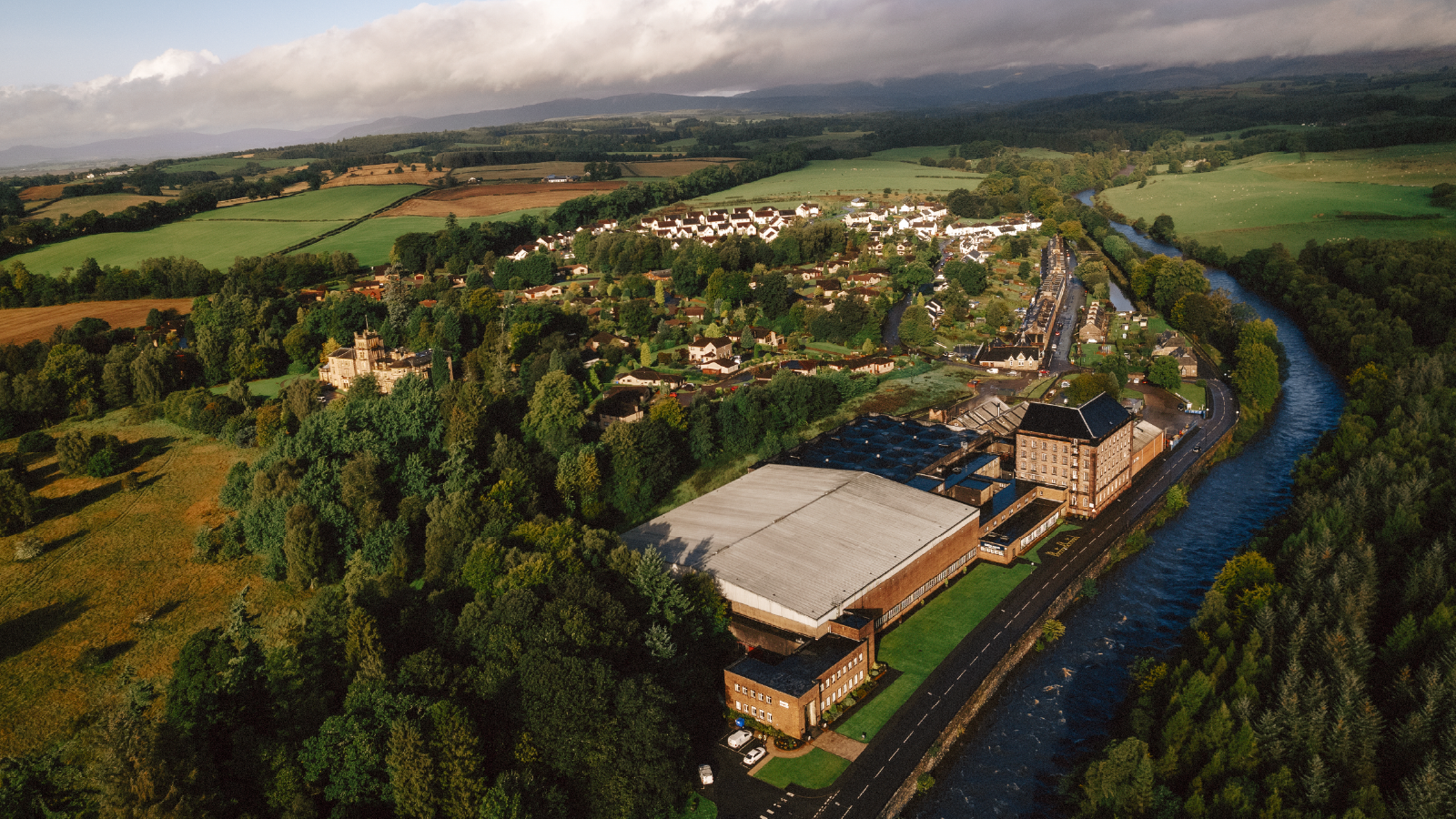 CVH Customer Story Illustrative Image 2 A scenic aerial view of a countryside distillery surrounded by green fields, a river, and a small village.