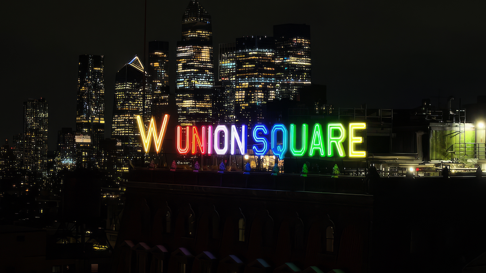 A colorful neon “Union Square” sign illuminated at night, with a city skyline of high-rise buildings in the background.