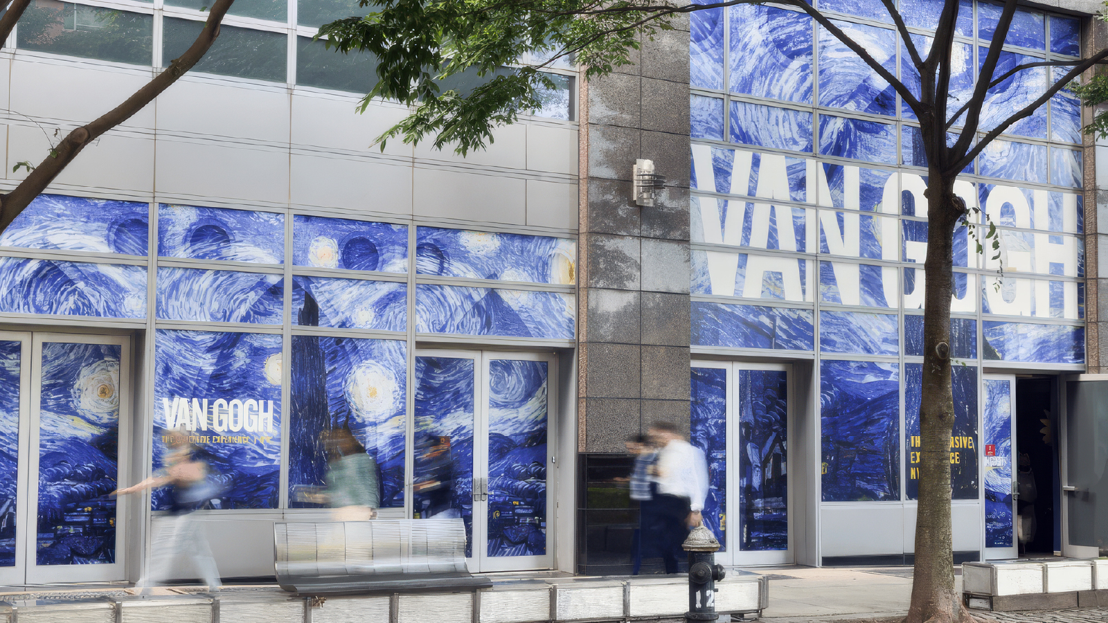 A building exterior featuring large window graphics of Vincent van Gogh’s artwork, with pedestrians walking past on the sidewalk.