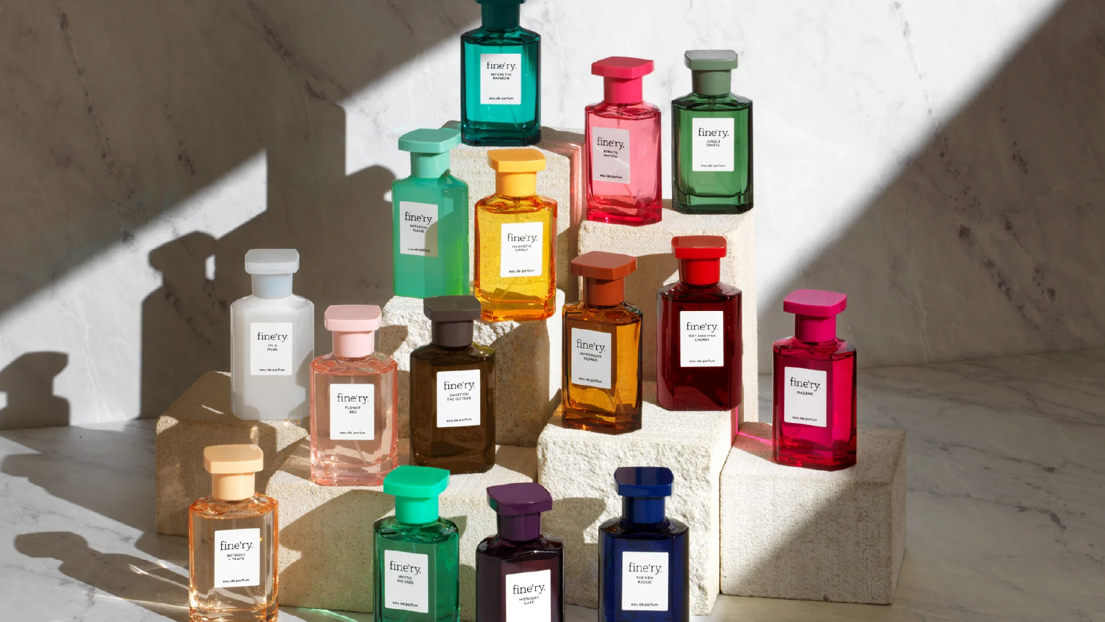 A collection of colorful glass perfume bottles arranged on stacked stone blocks, displayed in natural light against a neutral stone background.