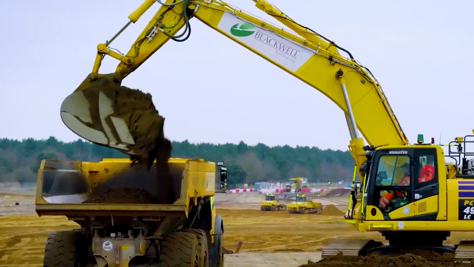 Sizewell C Customer Story Illustrative Image 1 A yellow excavator labeled “Blackwell Earthmoving” dumps soil into a large dump truck at a construction site with other machinery in the background.