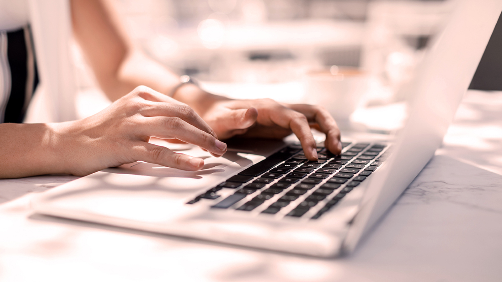 Nitto Denko Customer Story Illustrative Image 2 A close-up shot of hands typing on a laptop keyboard. The scene is well-lit, suggesting a bright workspace or outdoor setting.