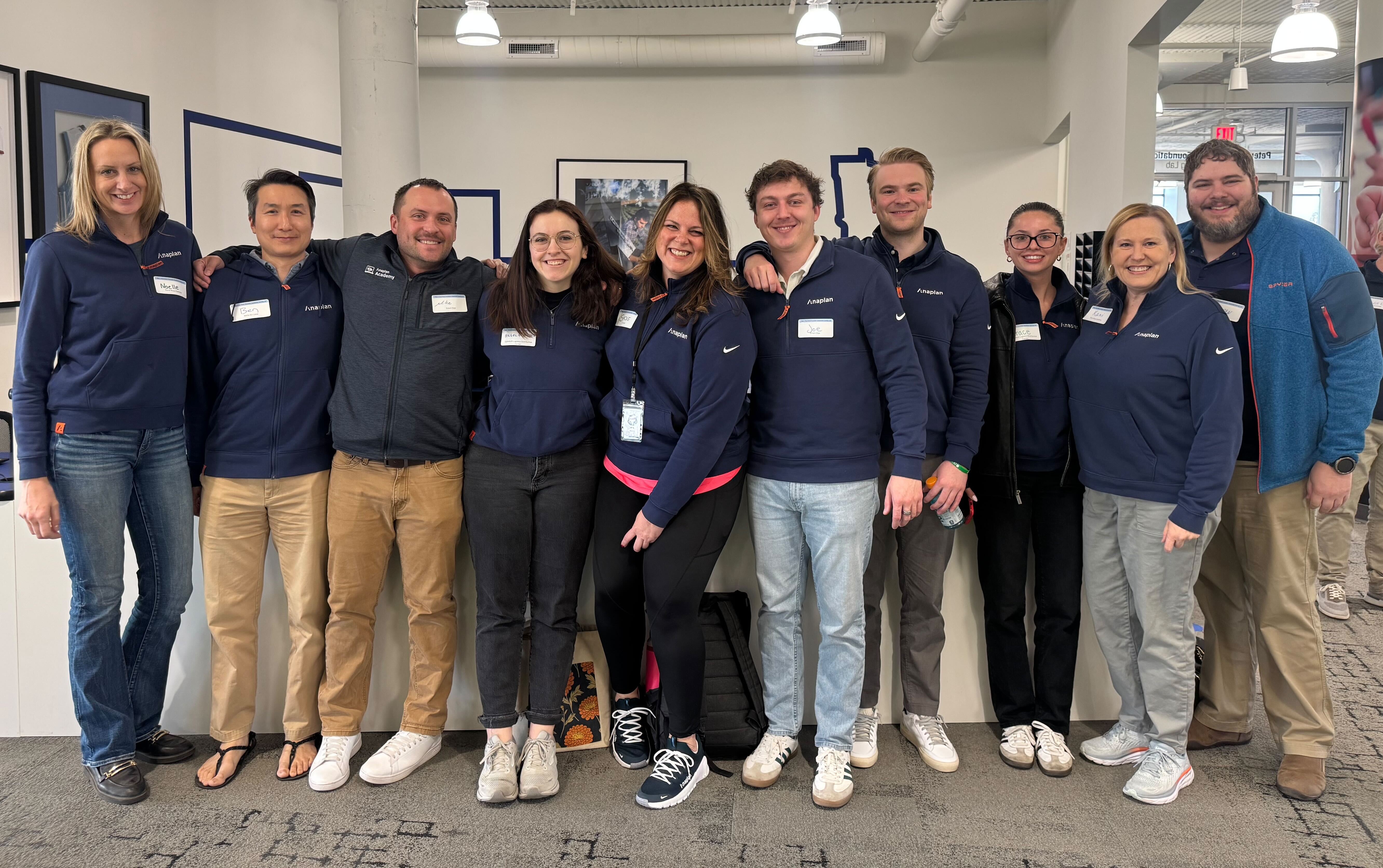 Group of Anaplan employees standing together indoors, smiling and posing for a team photo, representing collaboration and company culture.