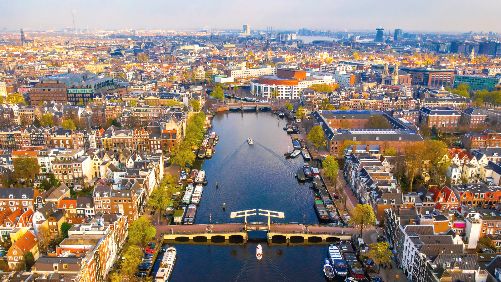 Aerial view of Amsterdam. Colorful cityscape showcasing canal boats, bridges, and traditional Dutch architecture under a bright sky.