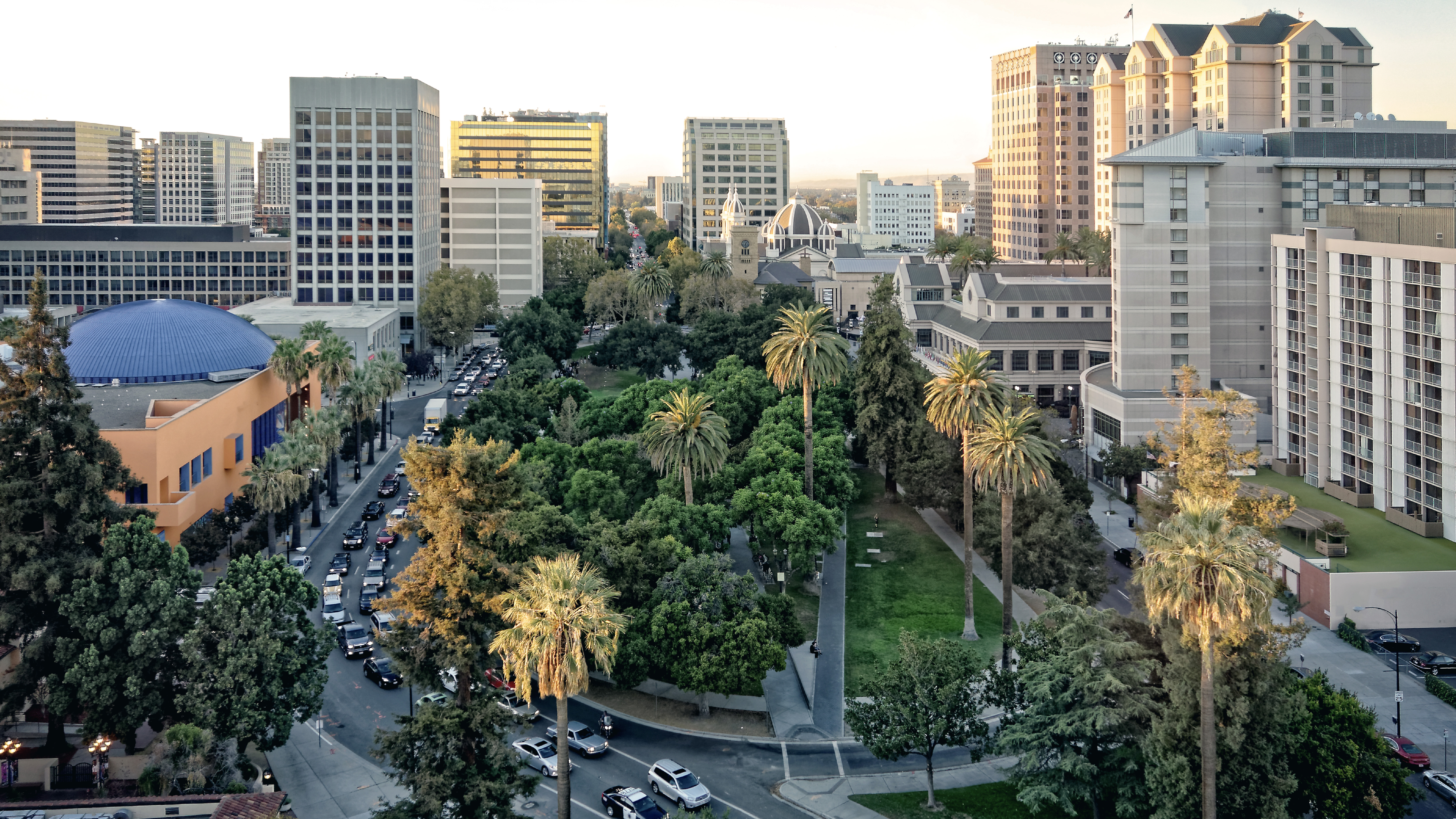 An aerial view of downtown San Jose featuring palm-lined streets, green park space, and surrounding mid-rise office buildings.