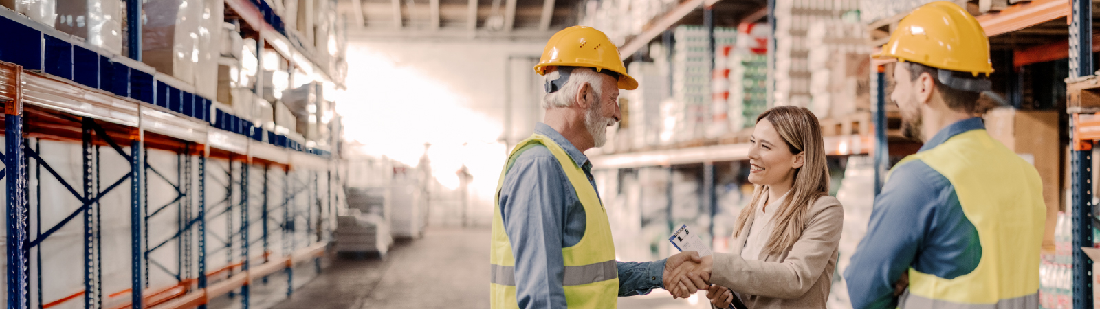 Woman shaking hands with warehouse worker in safety gear inside a stocked warehouse.