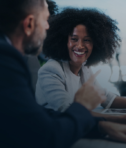 Two professionals in conversation during a business meeting, smiling and engaged, representing collaboration and strategic discussion.