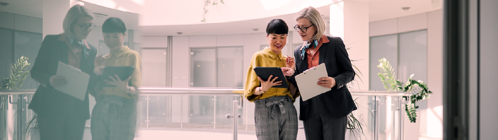 Two business professionals reviewing a tablet together in a modern office hallway with natural light.