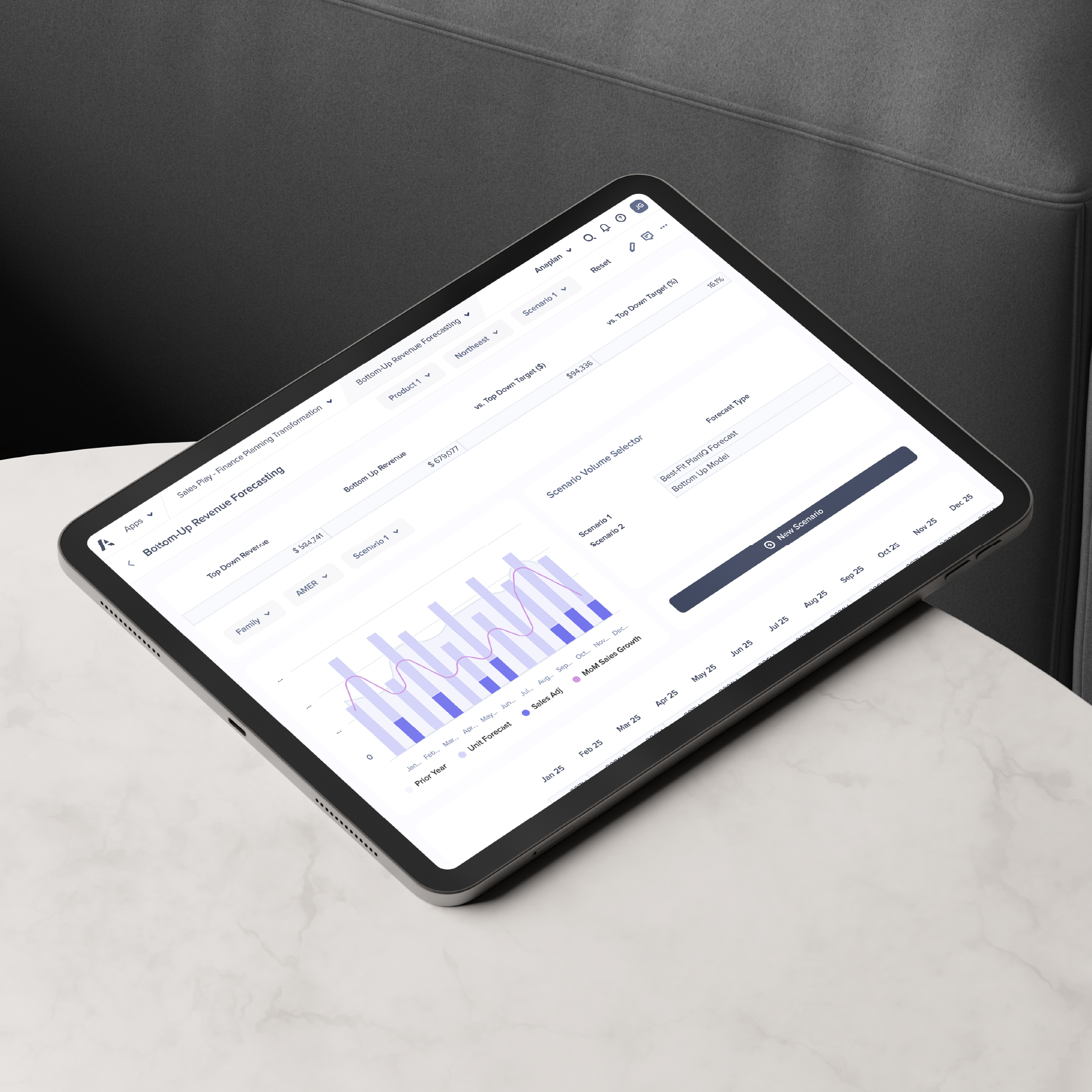 A tablet placed on a marble surface displays the Anaplan interface showing a bottom-up revenue forecasting dashboard with charts, scenario selectors, and sales growth data visualization.