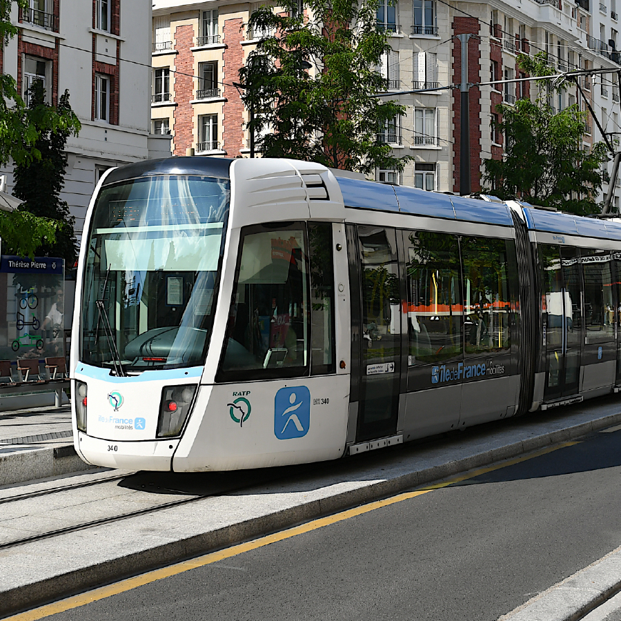 Modern white and blue tram with RATP and Île-de-France Mobilités logos stopped at a city tram station with buildings in the background.