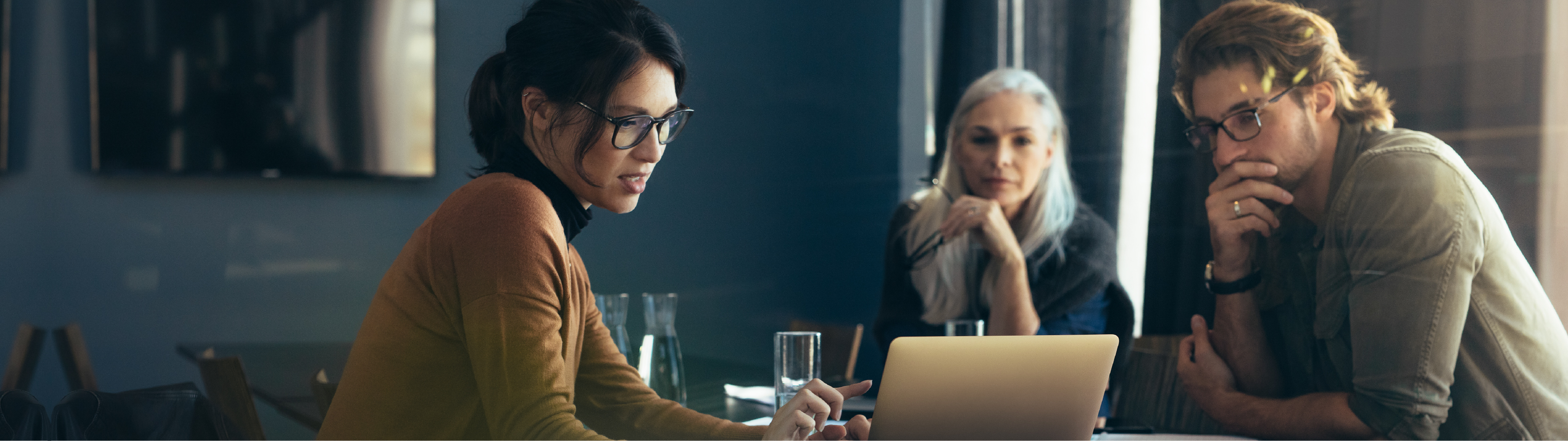 Three coworkers sitting at a table looking at a laptop