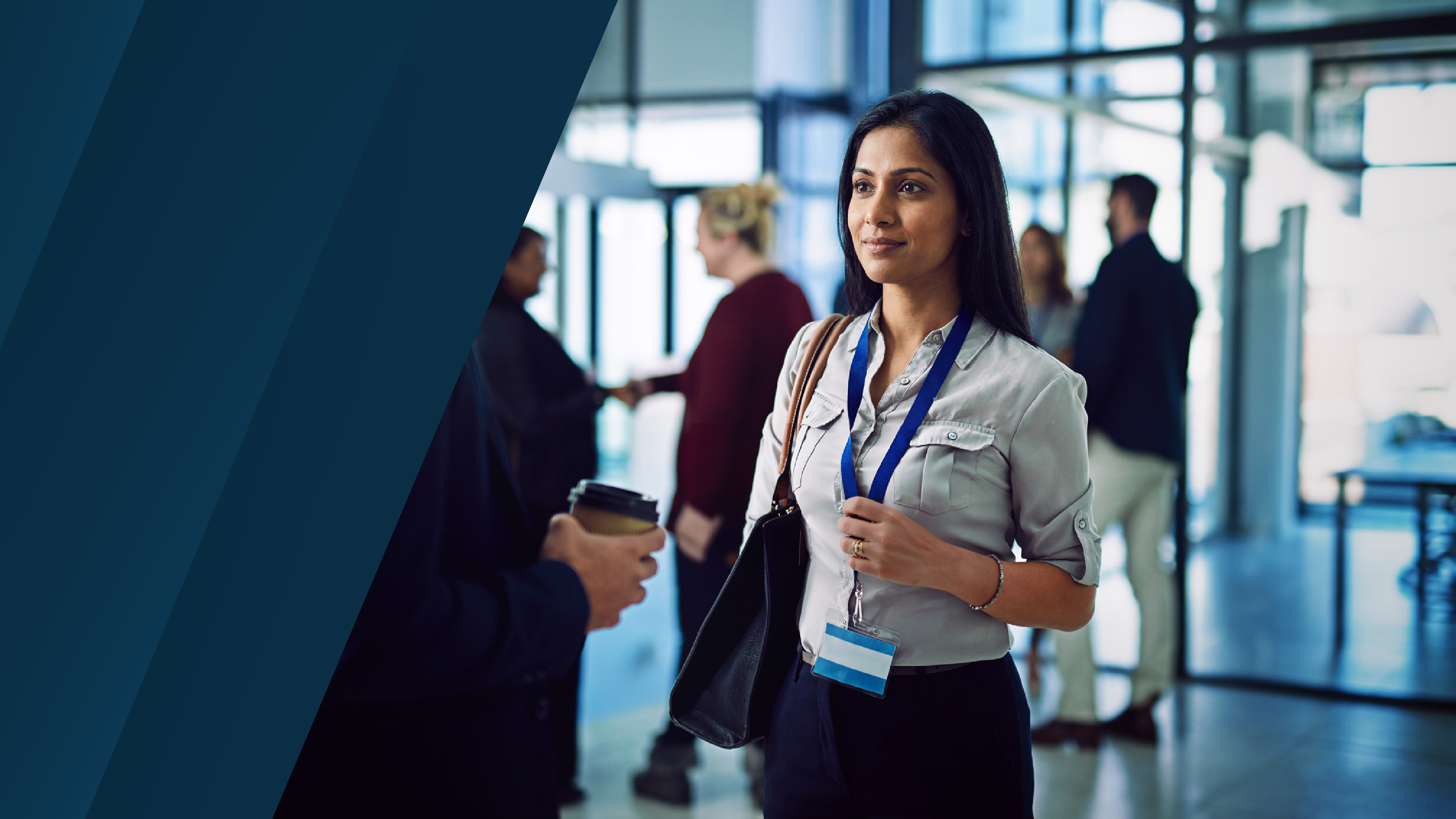 A business professional wearing a conference badge stands in a modern glass lobby while people converse in the background, with dark blue diagonal graphic panels on the left.