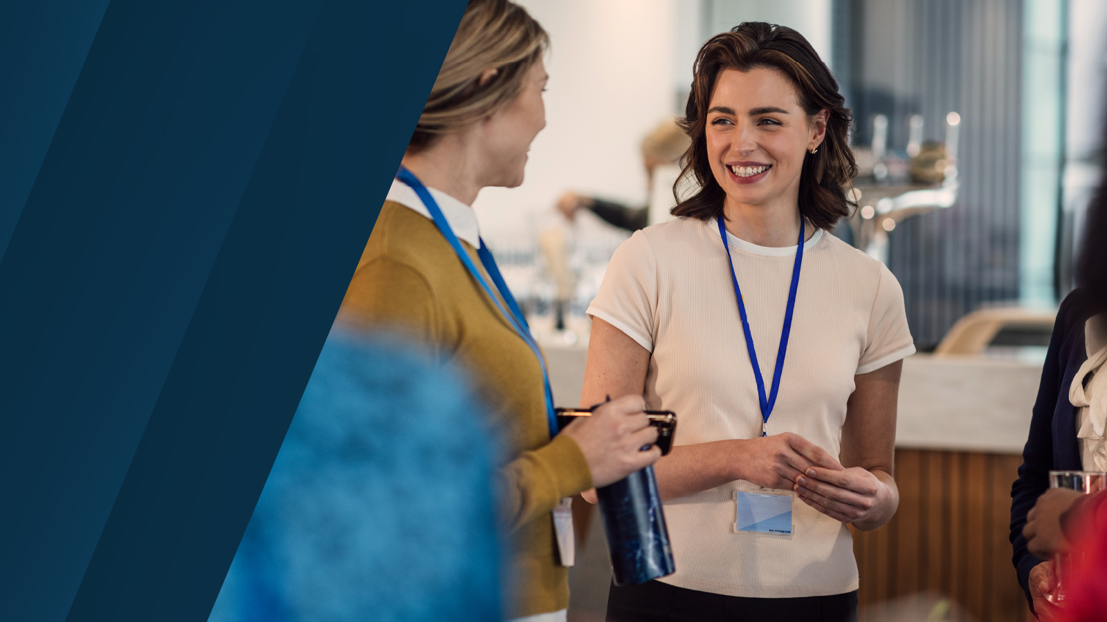 Professionals at a networking event talking and smiling, wearing conference badges and lanyards in a bright, modern event venue.