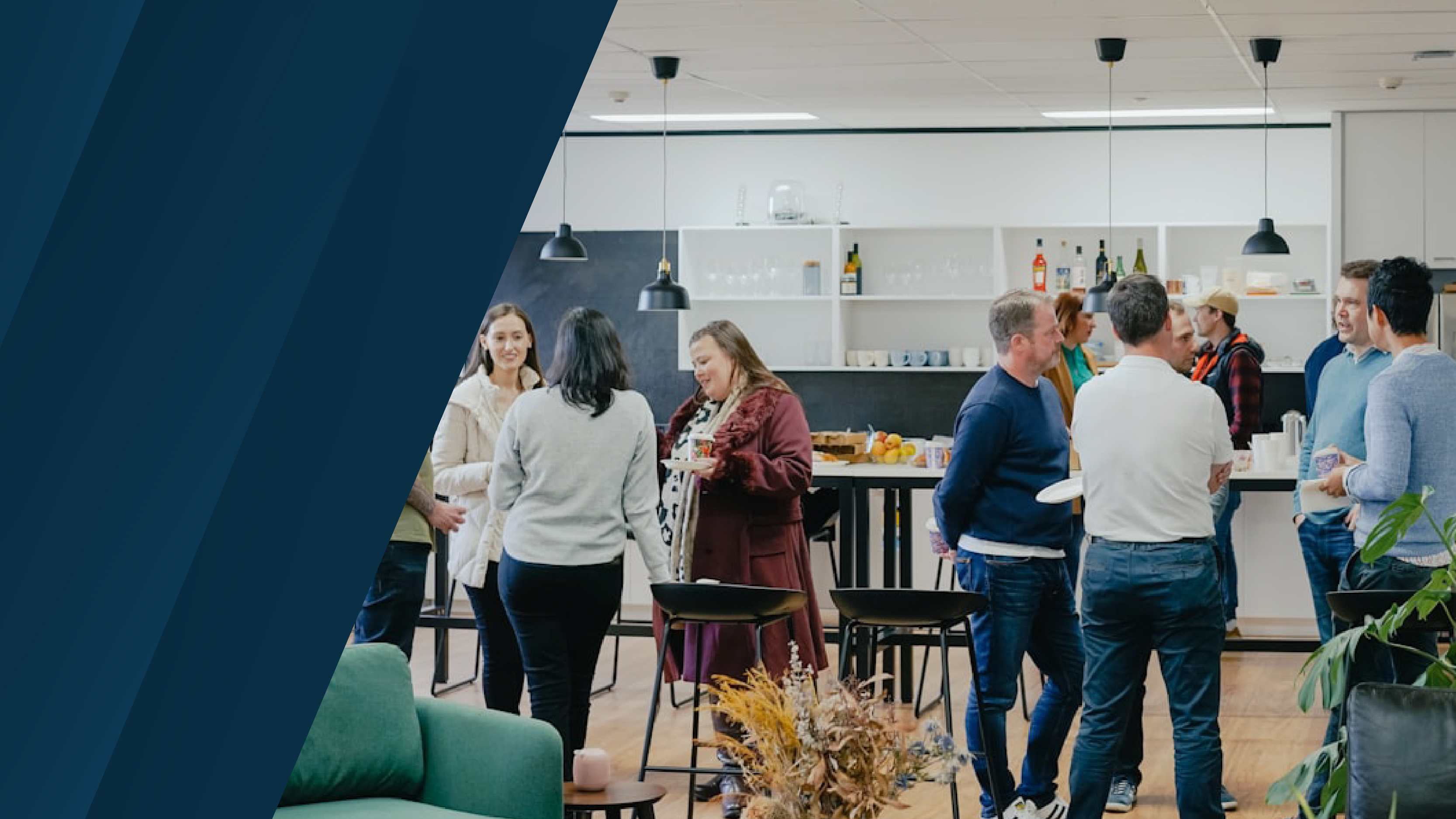 A group of professionals standing and conversing in a casual office lounge area with tables, chairs, and refreshments.