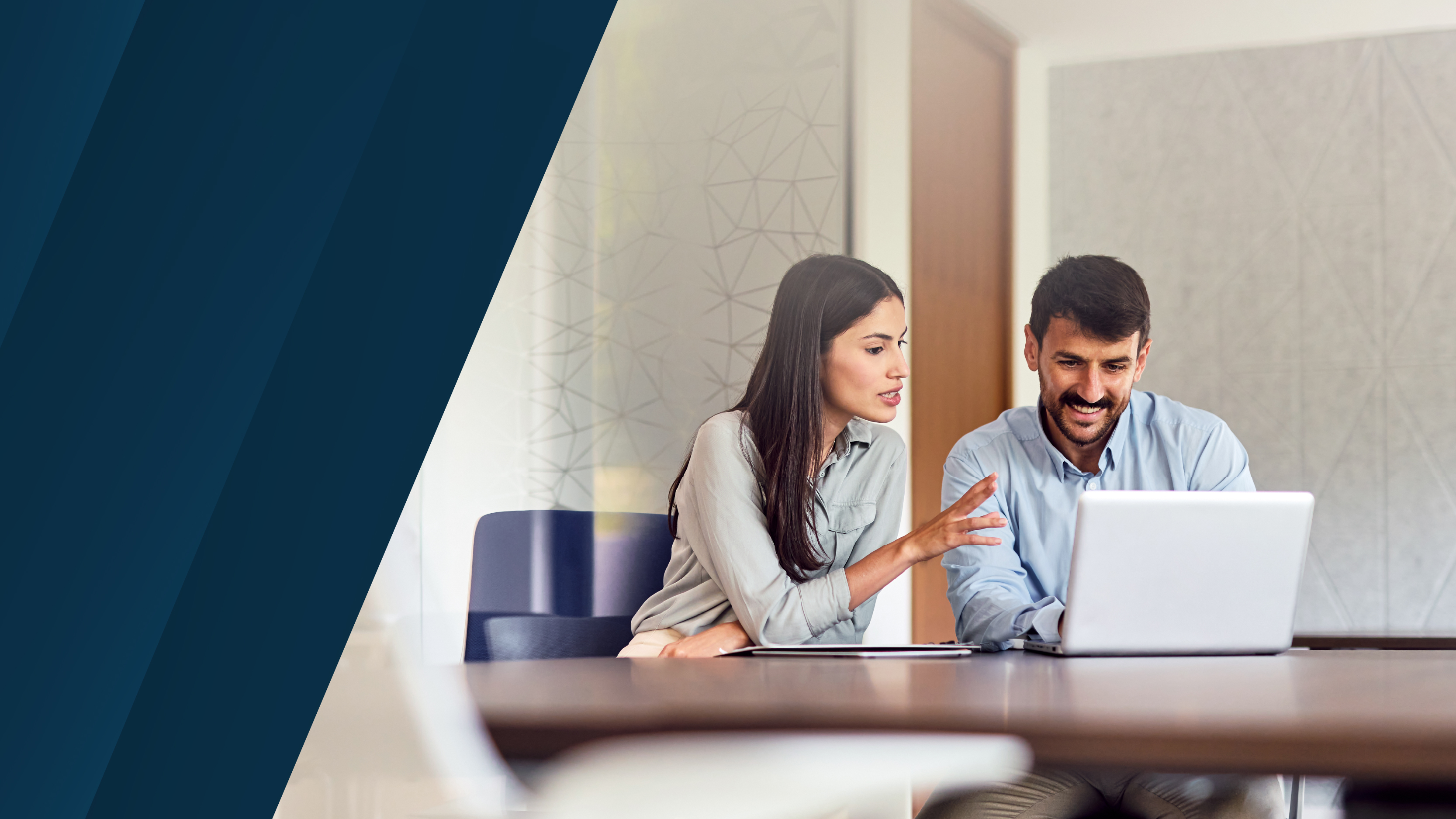 Deux professionnels assis à une table de réunion, discutant et consultant un ordinateur portable, représentant la collaboration et la planification financière.