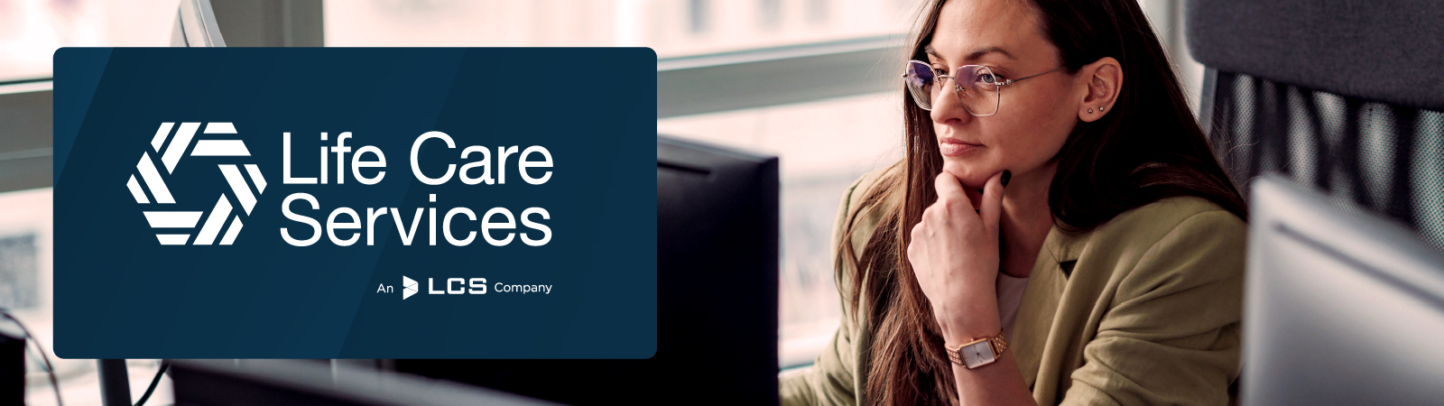 Life Care Services logo displayed on the left. A woman in glasses and a green blazer is seated at a desk in a modern office, concentrating on a computer screen.