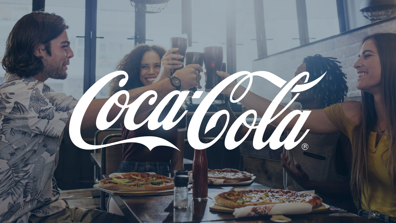Coca-Cola Logo displayed center. A group of friends cheers with drinks around a table with pizza at a casual restaurant.