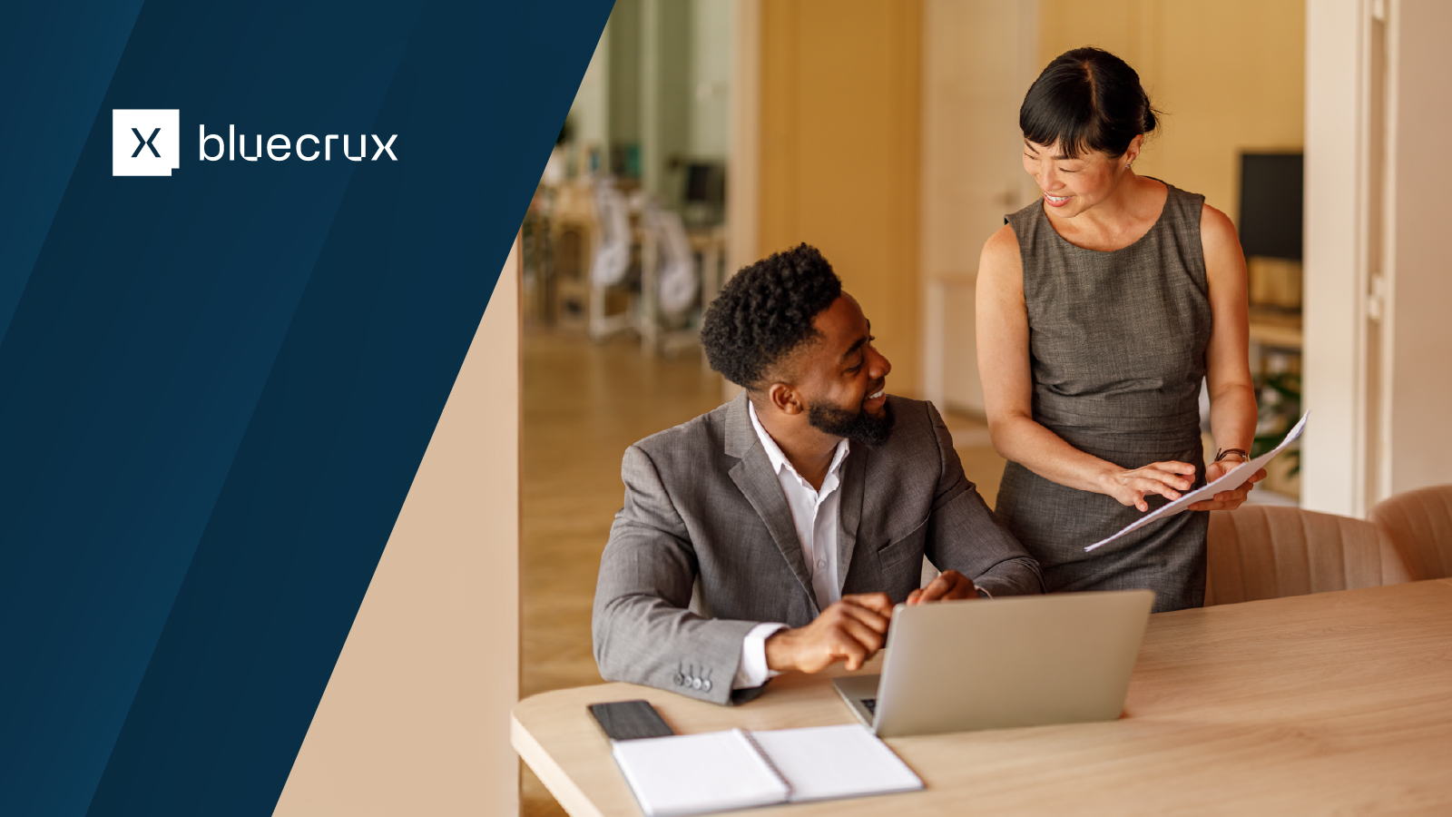 Bluecrux logo displayed on the left with an image of two professionals collaborating and reviewing a laptop and documents in a meeting setting.
