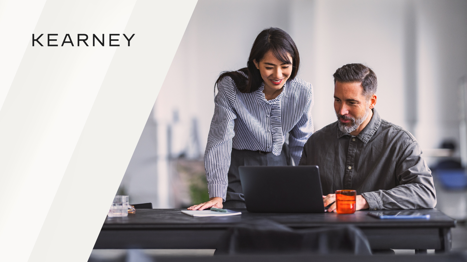 Two colleagues reviewing information on a laptop together at a desk in a modern office.