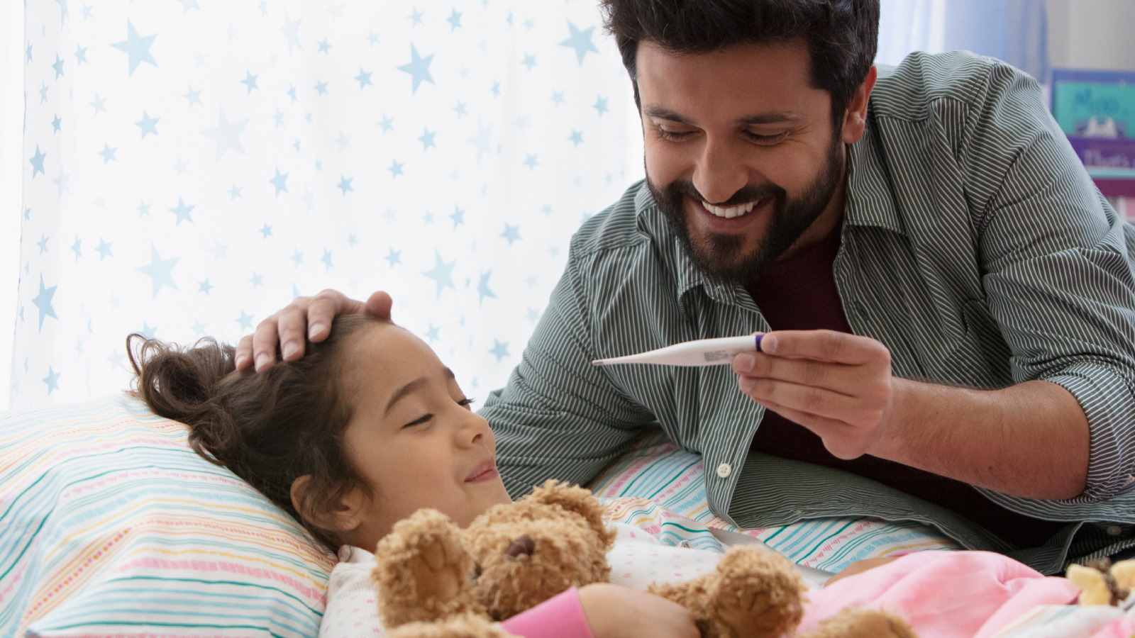 resources-customer-story-images-bayer-consumer-health Vater, der seiner Tochter den Kopf streichelt, während er auf ein Thermometer schaut