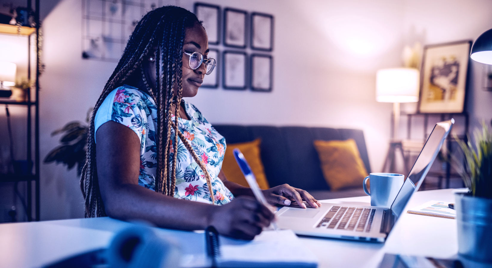 Woman working on laptop at desk and making notes