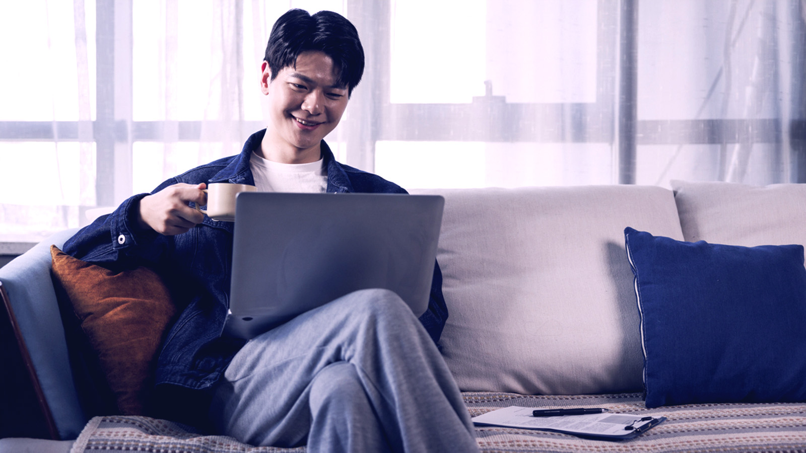 Man smiling on computer holding coffee while looking at laptop