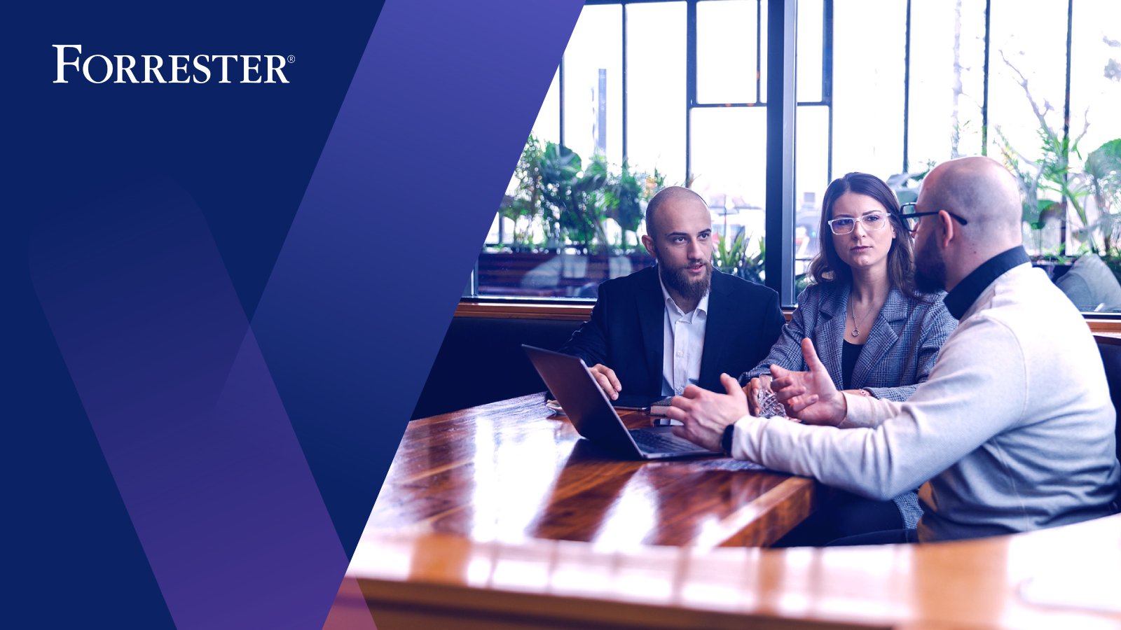 Three coworkers sitting at conference table having discussion around laptop