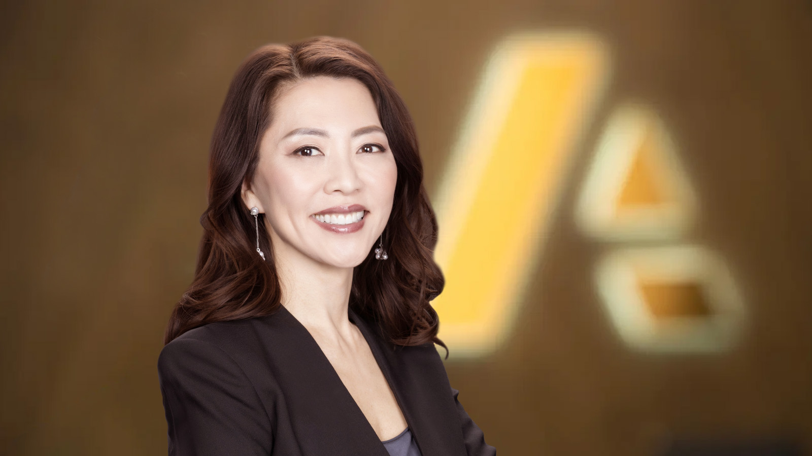 Businesswoman, Hyune Hand, Chief Customer Officer,  with shoulder-length hair curled, posing in front of Anaplan logo