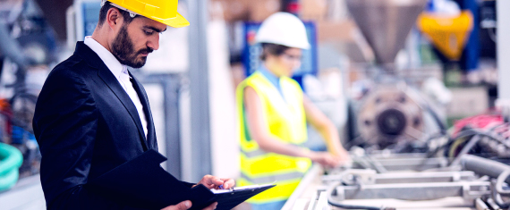 Hardhat wearing man in factory examining product on tablet