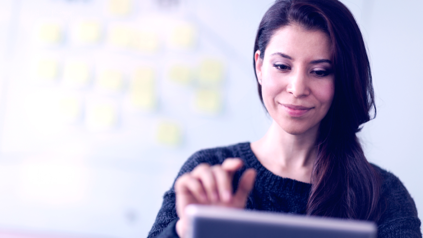 Business woman inputing into tablet with sticky notes on a whiteboard in the background