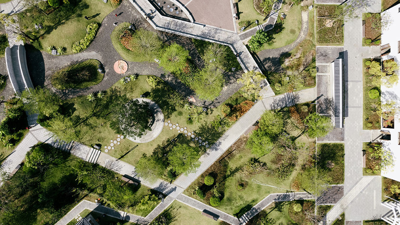 Aerial view of a landscaped park with winding paths, trees, and seating areas.