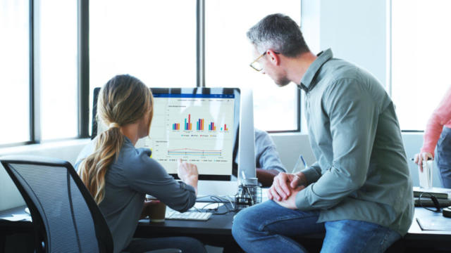 Two coworkers sitting together at a desk discussing a bar chart