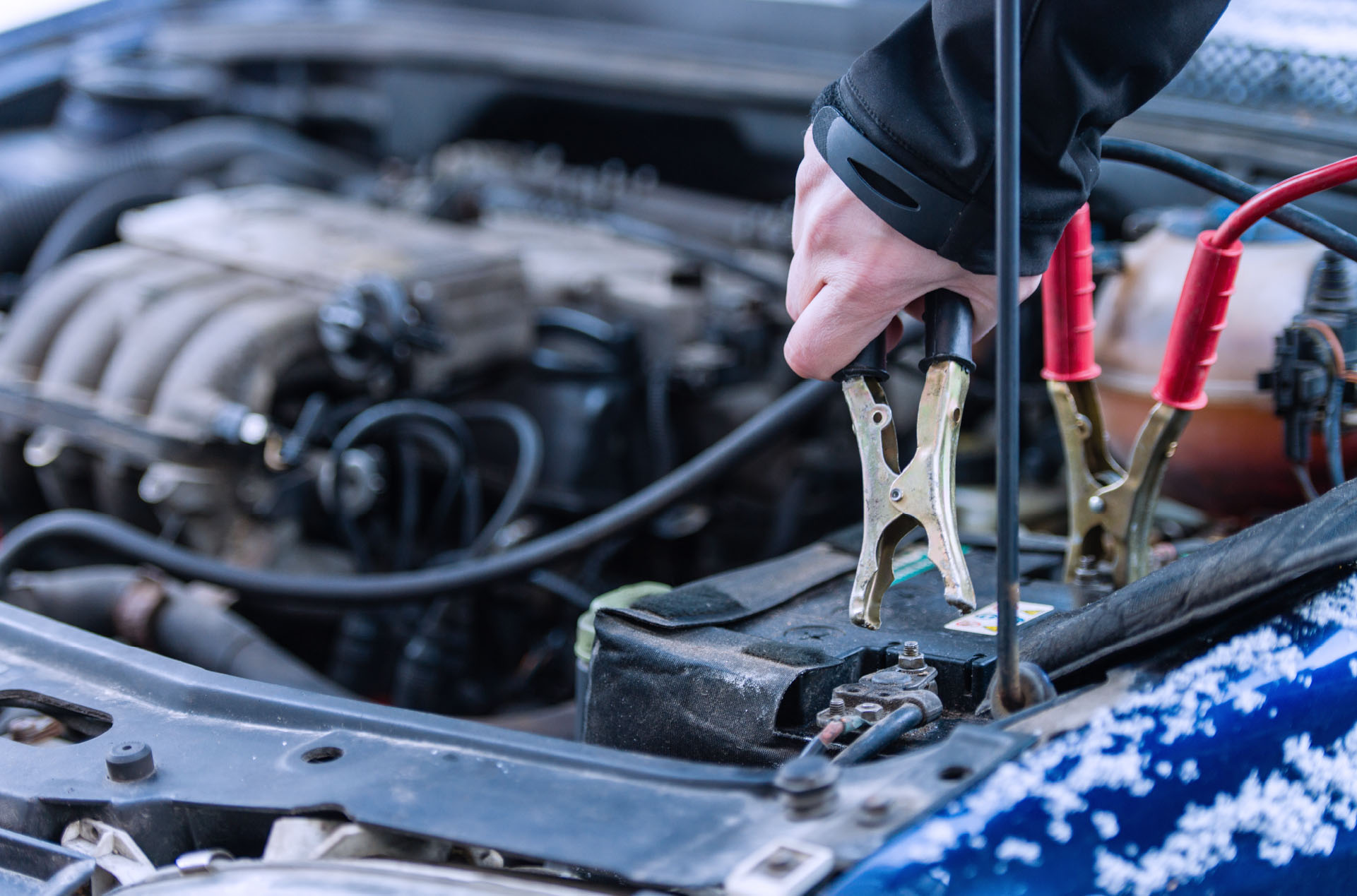 Person jump starting a car with electric cables