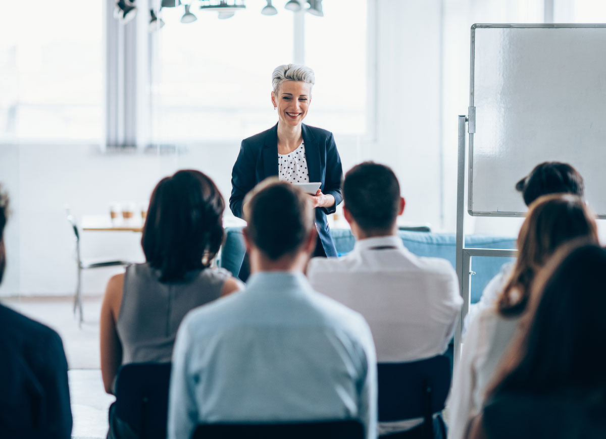 Woman addressing large gathering of colleagues during a presentation