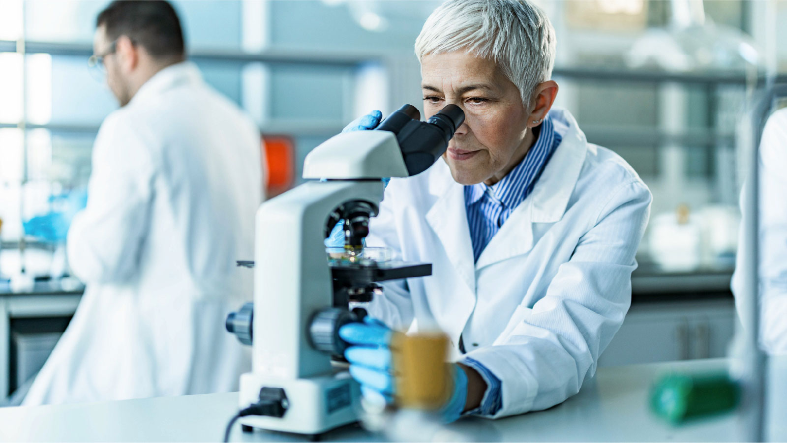 Scientist in lab examining sample through microscope