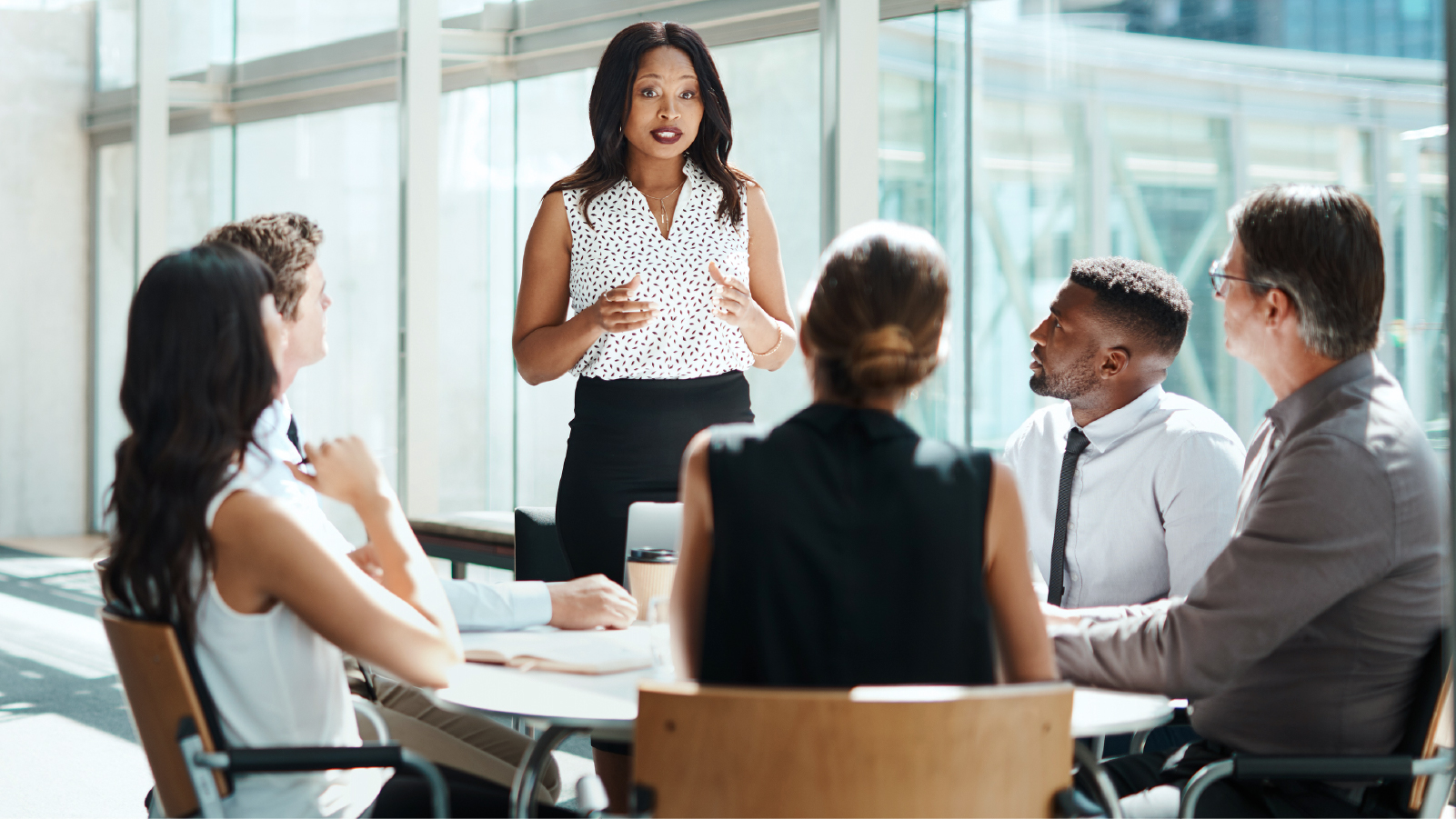 Woman standing and presenting to five seated coworkers at conference table