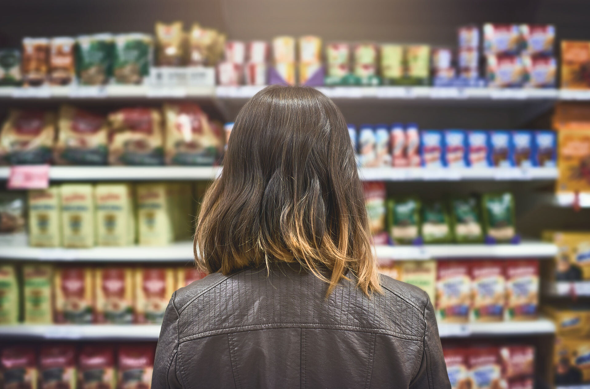 Back of woman's head looking at aisle of canned goods and other groceries  in store