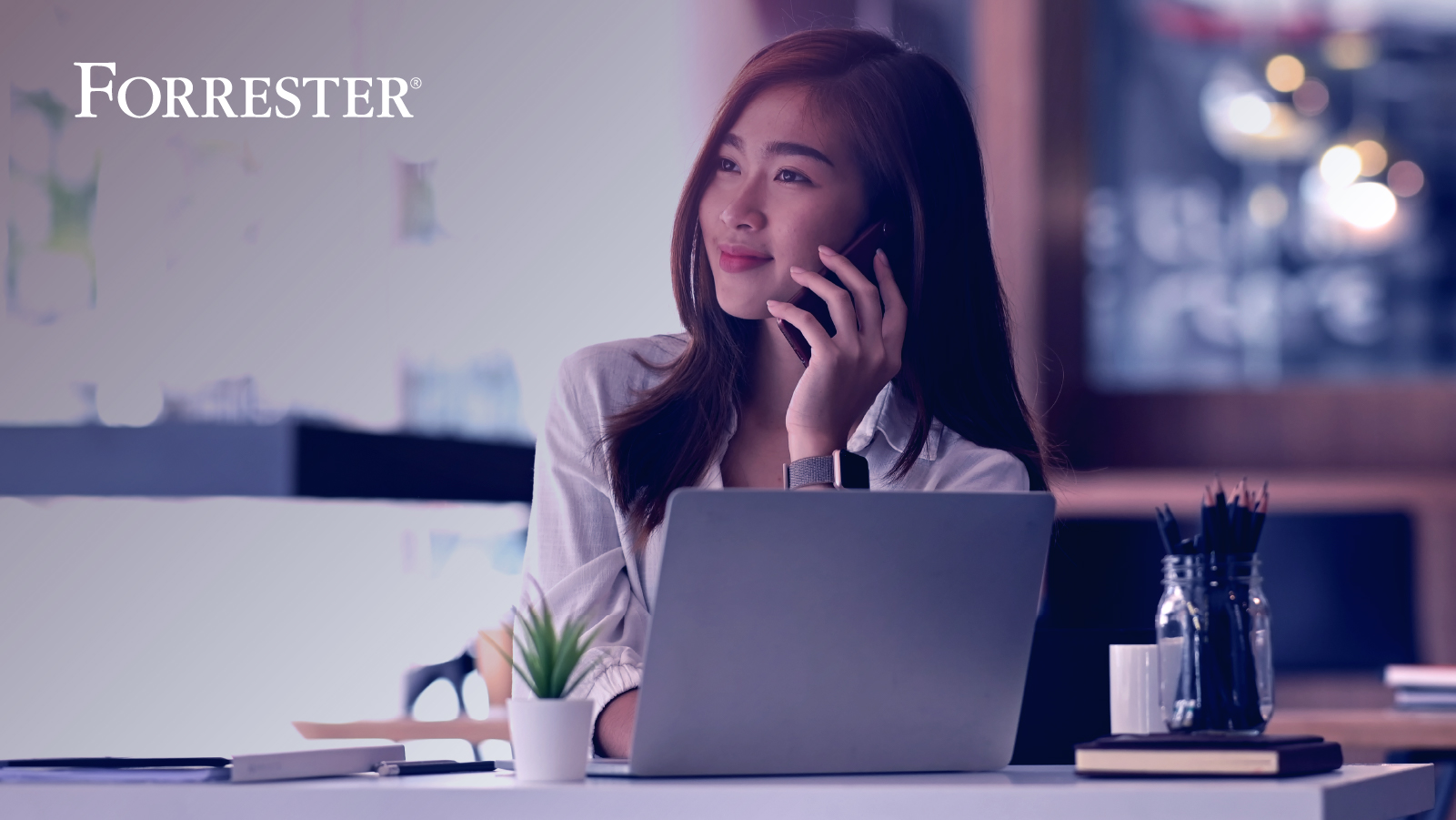 Woman smiling in front of laptop while talking on the phone and looking out window