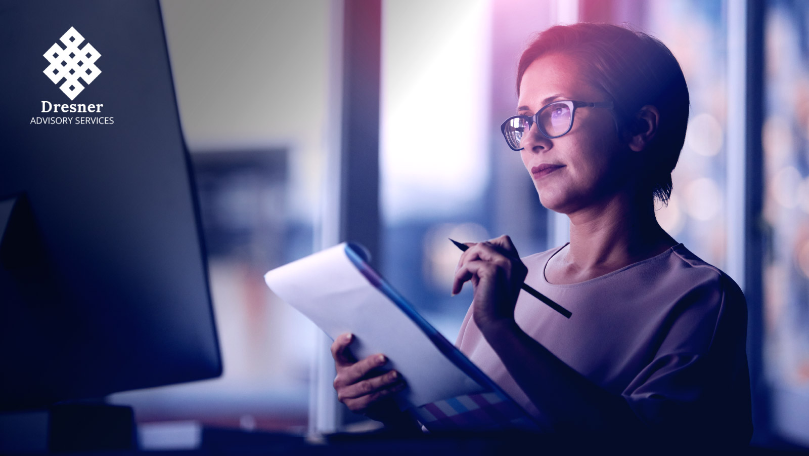 Woman looking at a computer screen while writing notes in a notepad