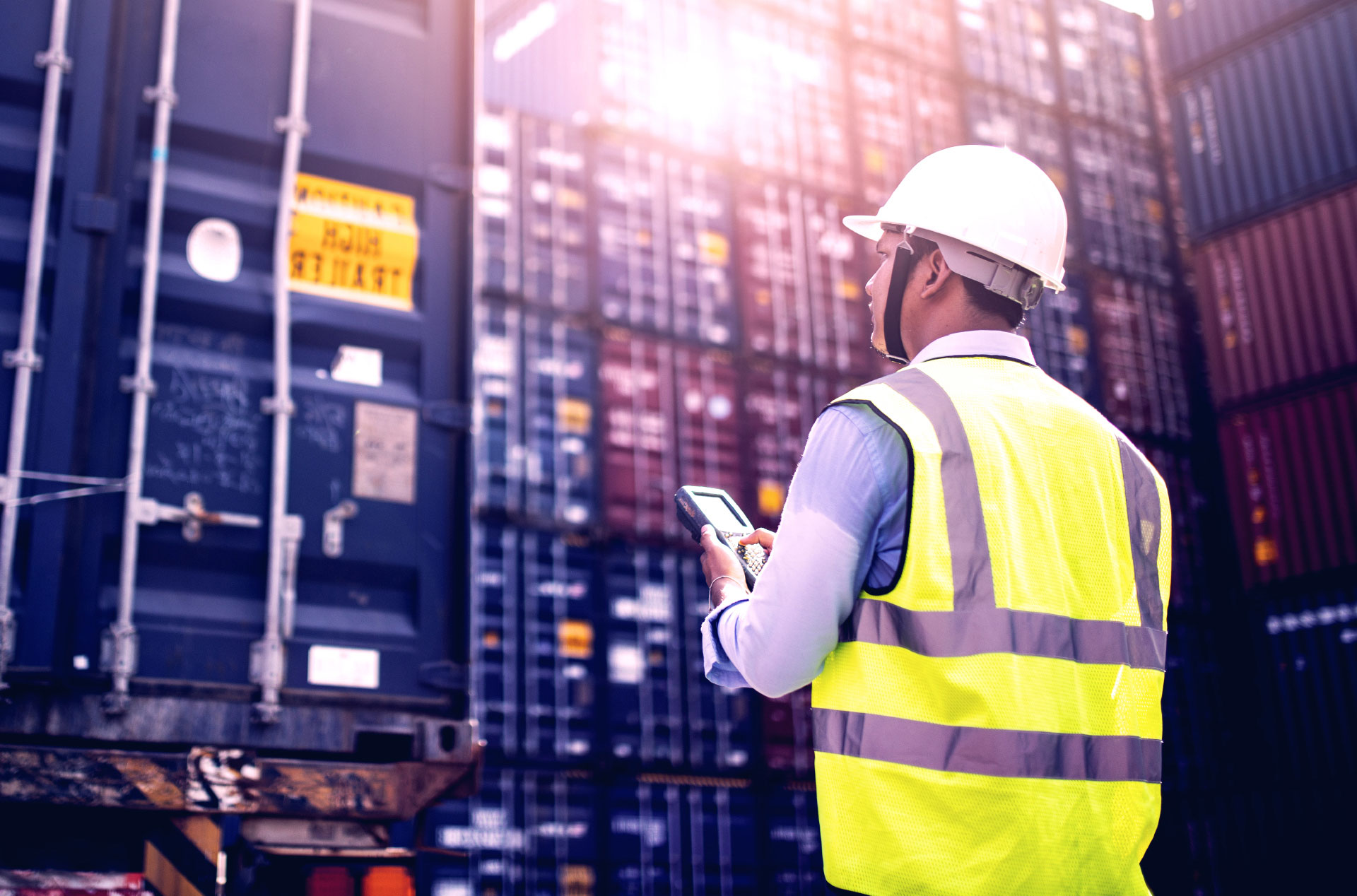 Man in a hard hat looking up at a large amount of freight containers